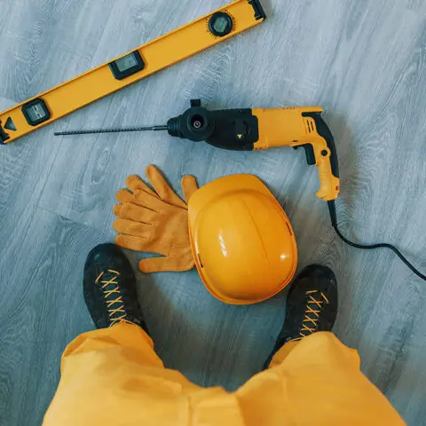 Handyman in yellow uniform with drill standing indoors. House renovation conception